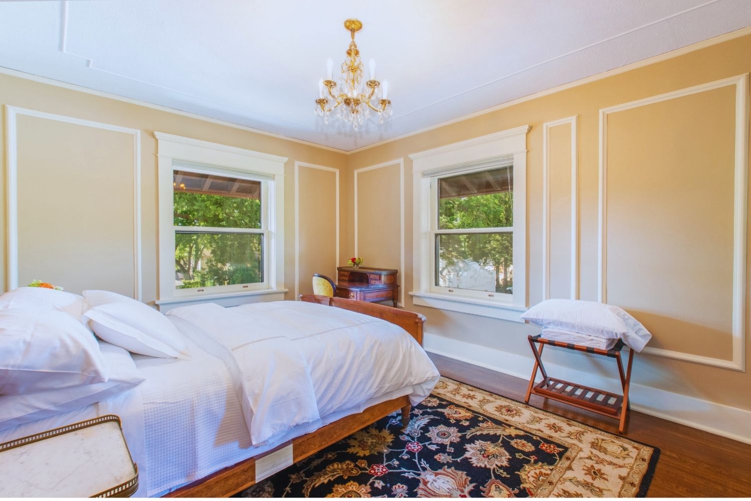 bright bedroom with beige walls, chandelier, wooden desk, and patterned rug at Martha’s Bed and Breakfast in Lincoln, Nebraska
