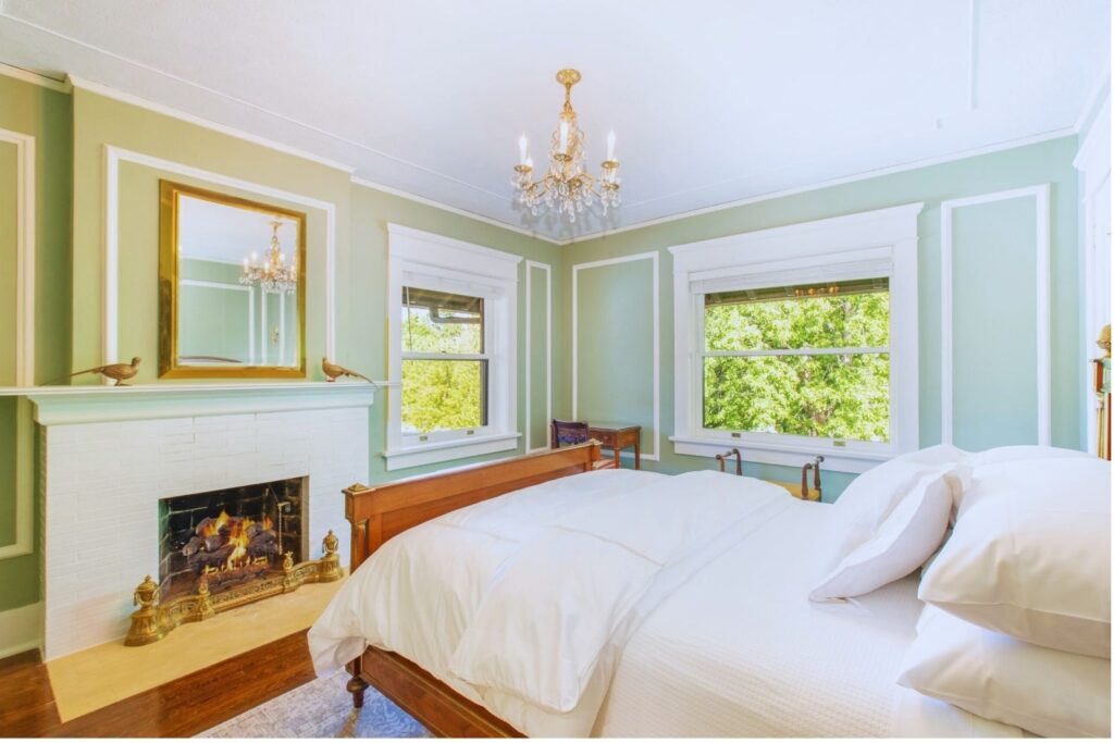 bright bedroom with white brick fireplace, gold-framed mirror, chandelier, and green walls at Martha’s Bed and Breakfast in Lincoln, Nebraska
