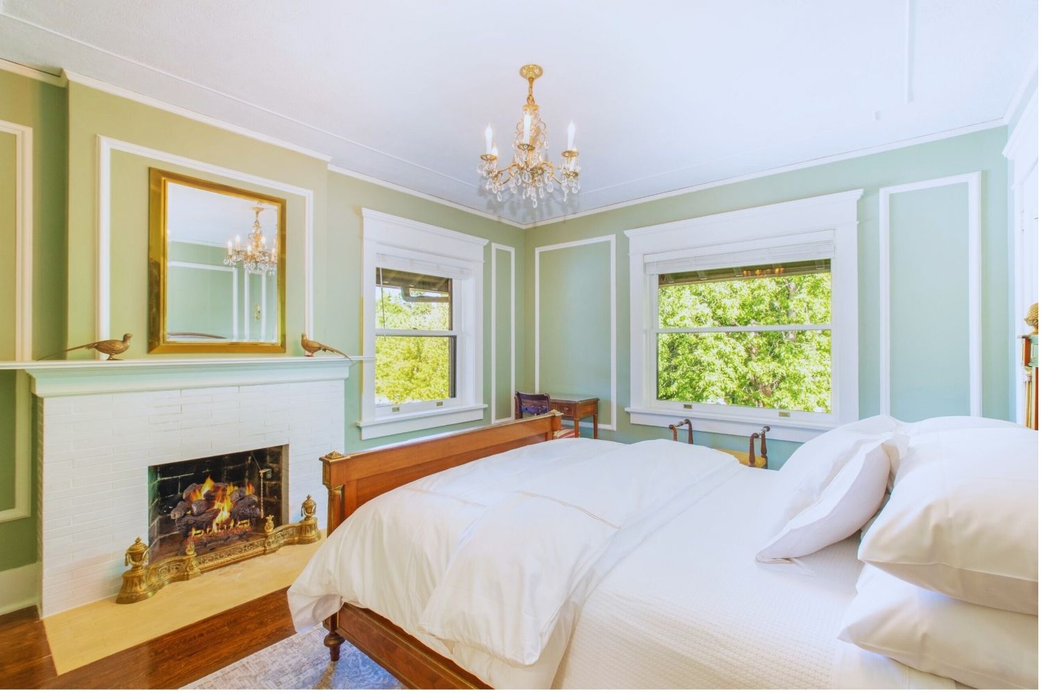 bright bedroom with white brick fireplace, gold-framed mirror, chandelier, and green walls at Martha’s Bed and Breakfast in Lincoln, Nebraska