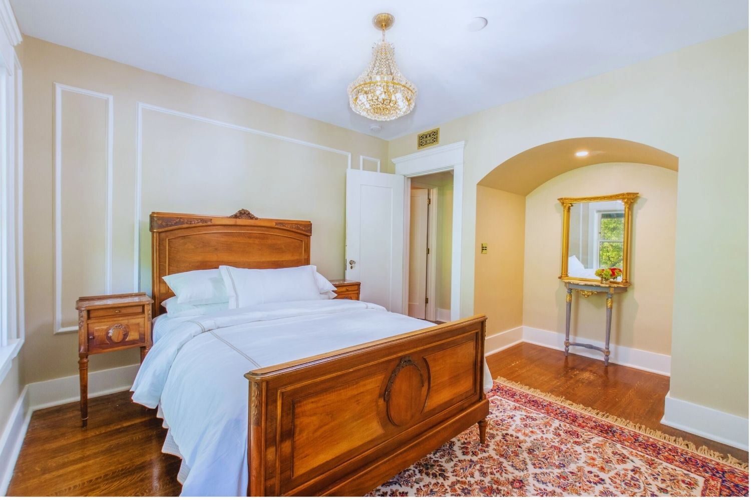 elegant bedroom with carved wooden bed, chandelier, arched alcove, and gold-framed mirror at Martha’s Bed and Breakfast in Lincoln, Nebraska