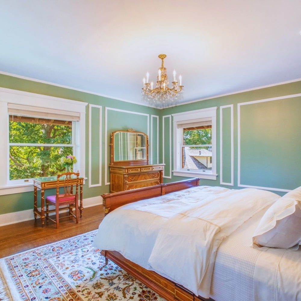 Elegant vintage-style bedroom with green walls, antique furniture, and chandelier at Martha's Bed and Breakfast in Lincoln, Nebraska